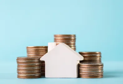 monety poukładane w słupki na tle białego domu 